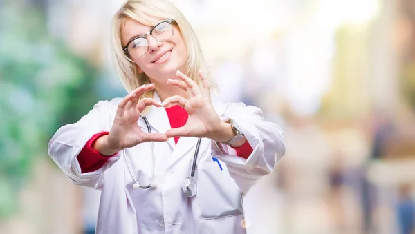 年轻美丽的金发医生妇女穿着医疗制服在孤立的背景下微笑着爱显示心脏符号和形状与手 浪漫理念 — 图库照片
