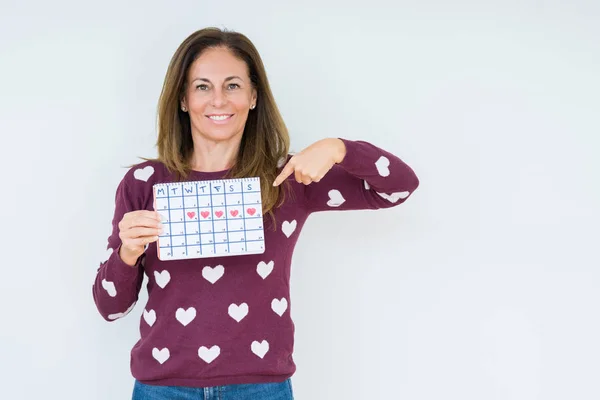 Middle age woman holding menstruation calendar over isolated background with surprise face pointing finger to himself