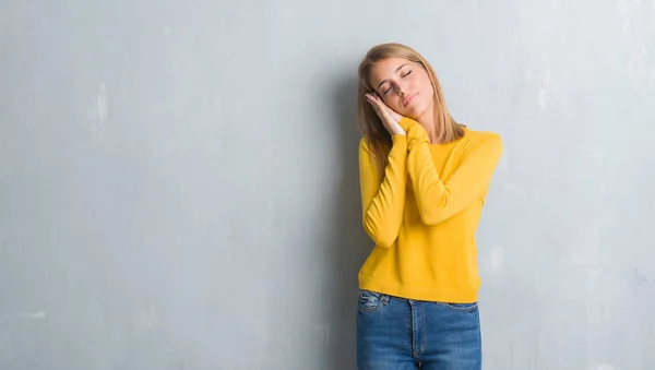 美丽的年轻女子站在咕深光灰色的墙壁上睡累的梦和摆姿势 双手放在一起 而微笑着闭着眼睛 — 图库照片