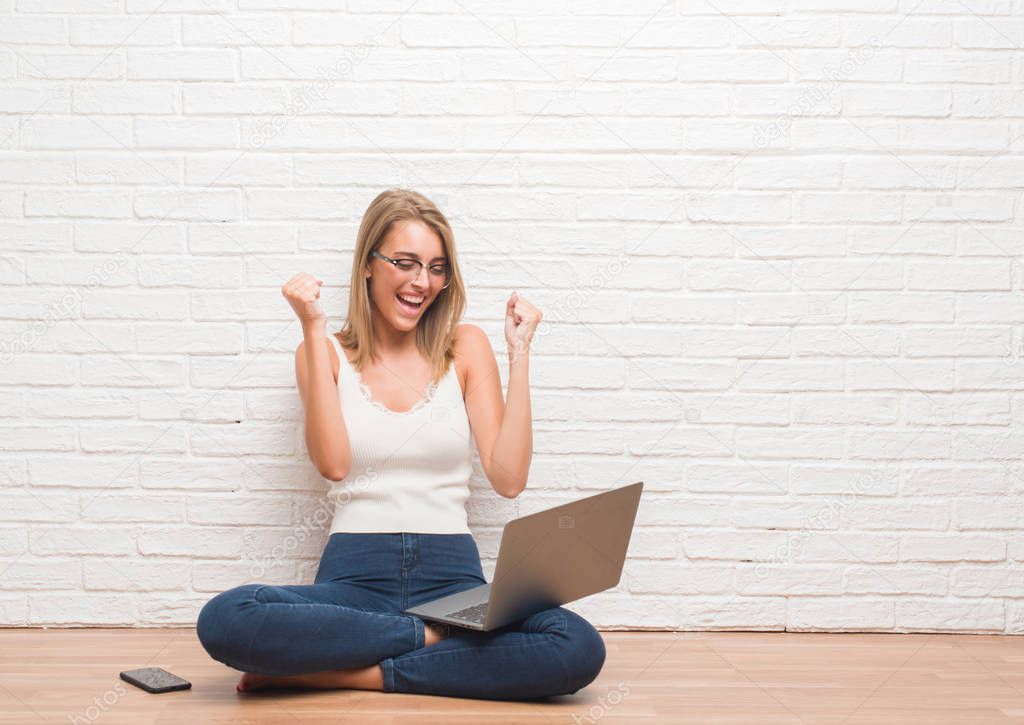 Beautiful young woman sitting on the floor working using laptop at home screaming proud and celebrating victory and success very excited, cheering emotion