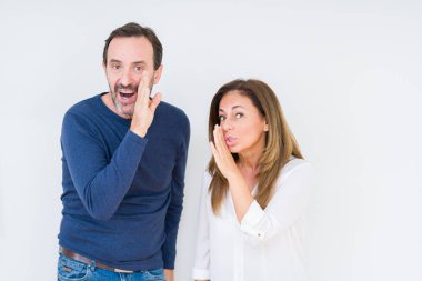 Beautiful middle age couple in love over isolated background hand on mouth telling secret rumor, whispering malicious talk conversation