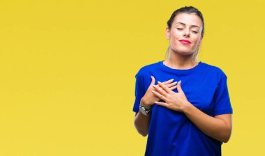 Genç güzel kadın ile gülümseyen izole arka plan üzerinde rahat mavi t-shirt giyen kapalı gözler ve yüzünde minnettar jest ile göğüs üzerinde eller. Sağlık kavramı.
