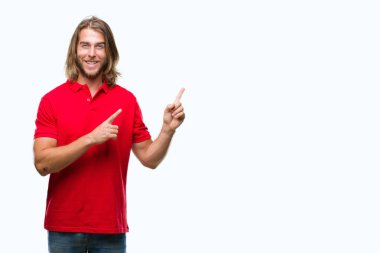 Gülümseyen ve iki elleri ve parmakları ile tarafına işaret kamera bakarak izole arka plan üzerinde uzun saçlı yakışıklı delikanlı.