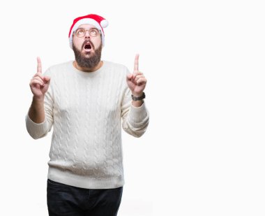 Noel şapka ve gözlük izole arka plan üzerinde giyen genç beyaz adam hayret ve yukarıya bakıp parmakları ile işaret şaşırttı ve silah kaldırdı.