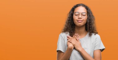 Gözlüklü kapalı gözler ile göğüs ellerinde ve yüzünde minnettar jest ile gülümseyen güzel genç İspanyol kadın. Sağlık kavramı.