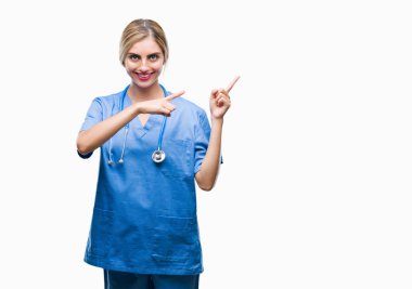 Genç güzel sarışın doktor cerrah hemşire kadın gülümseyerek ve iki elleri ve parmakları ile tarafına işaret kamera bakarak izole arka plan.