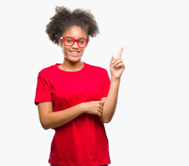 Kameraya bakarak yan el ve parmak ile işaret yüzünde kocaman bir gülümseme ile izole arka plan üzerinde gözlük takan genç afro Amerikalı kadın.