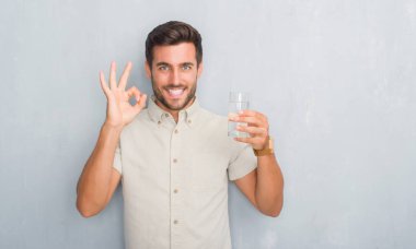 Parmak, mükemmel sembolü ile ok işareti yapıyor su içme gri grunge duvarın üzerinden yakışıklı genç