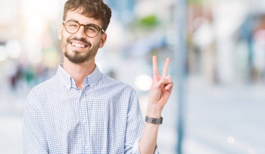 Mutlu yüz zafer işareti yaparken kameraya göz kırpıyor ile gülümseyen izole arka plan üzerinde gözlük takan yakışıklı delikanlı. İki numaralı.