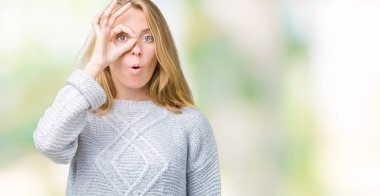 Sürpriz yüz, göz parmaklarının arasından seyir ile ok jest yapıyor izole arka plan üzerinde kış kazak giyen güzel genç kadın şok. İmansız ifade.