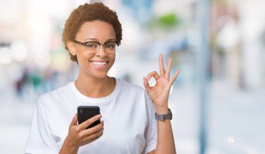 Parmak, mükemmel sembolü ile ok işareti yapıyor izole arka plan üzerinde akıllı telefon kullanan genç Afro-Amerikan kadın