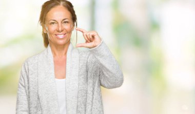 İzole arka plan gülümseyen ve boyutu işaret parmaklı ararken ve kamera işi el ile kendinden emin eller üzerinde kış kazak giyen güzel orta yaş yetişkin kadın. Ölçü kavramı.