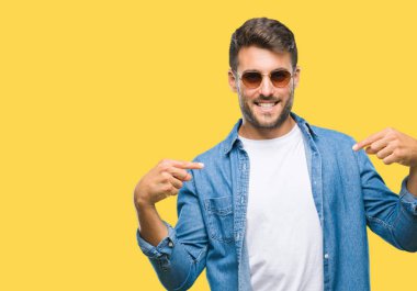 Yakışıklı delikanlı yüzünde gülümseme ile kendinden emin görünüyorsun, kendini gururlu ve mutlu parmakları ile işaret izole arka plan üzerinde güneş gözlüğü takıyor.
