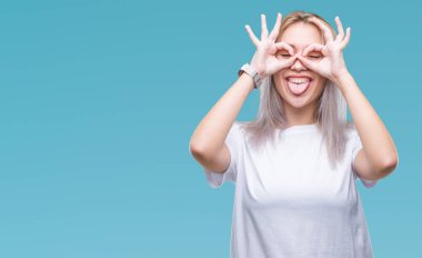 Genç Sarışın kadın dilini, parmaklarının arasından baktığını yapışmasını dürbün gibi ok jest yapıyor izole arka plan yüzünden. Deli ifade.