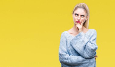 Kadın giyiyor kış kazak üzerinde arka plan ile ilgili soru, dalgın ifade düşünme çene yandan izole genç güzel sarışın ve mavi gözlü. Düşünceli yüzüyle gülümsüyor. Şüphe kavramı.