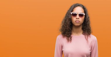 Güzel genç İspanyol kadın yüzünde ciddi bir ifade ile güneş gözlüğü takıyor. Basit ve doğal kameraya bakıyor.