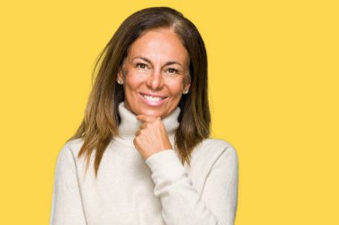 Emin çapraz kollar ve çeneme kaldırdı el ile gülümseme ile kameraya bakarak izole arka plan üzerinde kış kazak giyen güzel orta yaş yetişkin kadın. Pozitif düşünce.