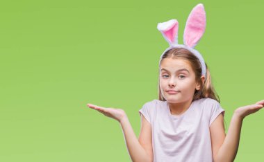 Paskalya bunny kulaklar izole arka plan clueless ve şaşkın bir ifadeyle kollar ve eller kaldırdı üzerinde giyen genç güzel kız. Şüphe kavramı.