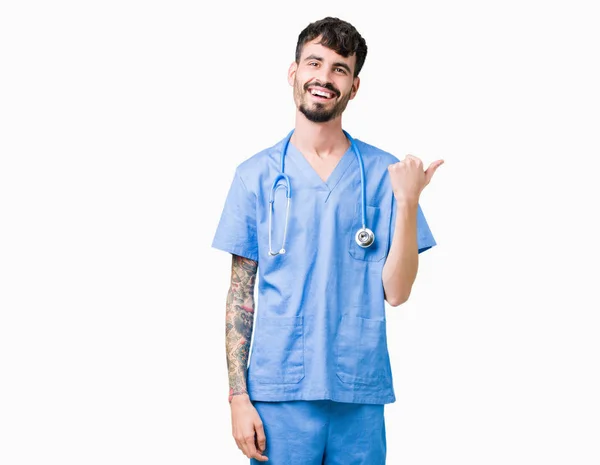 看護師の若いハンサムな男を探していると親指側に上向きの幸せそうな顔を浮かべて孤立の背景の上の外科医の制服を着て — ストック写真