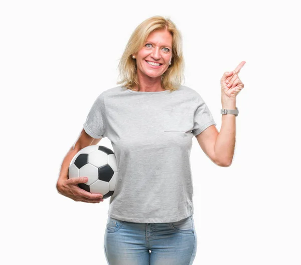 中年金发女子举行足球足球在孤立的背景非常高兴地指着手和手指的侧面 — 图库照片