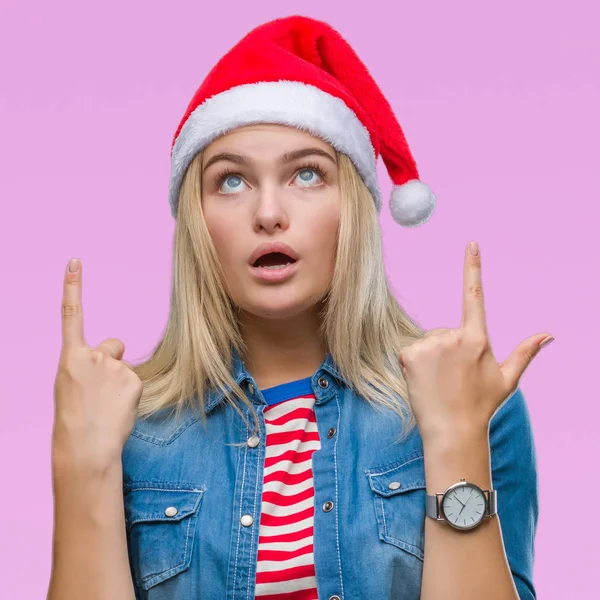 若い白人女性隔離された背景にクリスマスの帽子をかぶってびっくり驚いて見上げると指で指していると腕を上げた — ストック写真