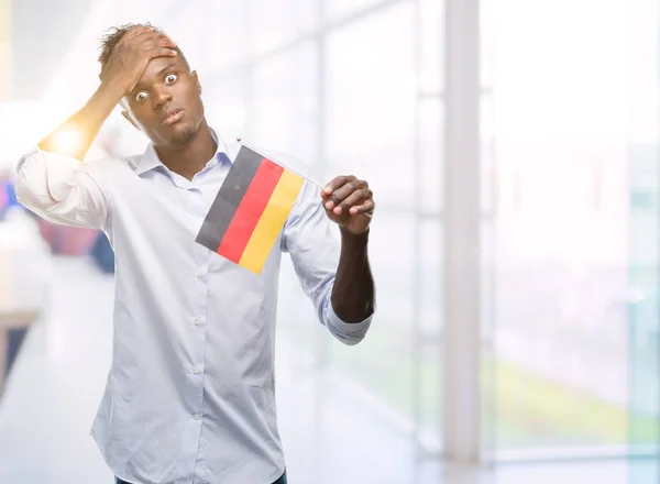 驚きの恥とショックの頭の上の手を強調した若いアフリカ系アメリカ人持株のドイツの旗の顔 怒っているとイライラ 恐怖と動揺の間違い — ストック写真