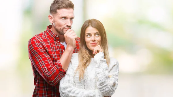 Aşık üzerinde kış kazak giyen genç çift çene düşünme hakkında soru, dalgın ifade üzerine el ile arka plan izole. Düşünceli yüzüyle gülümsüyor. Şüphe kavramı.
