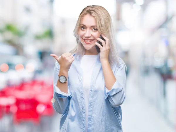 Mladá Blond Žena Mluví Prostřednictvím Smarpthone Přes Samostatný Pozadí Ukazuje — Stock fotografie