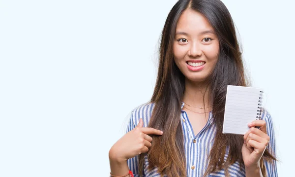 自分自身に驚き顔ポインティング指で孤立した背景の上のノートを保持している若いアジア女性 — ストック写真