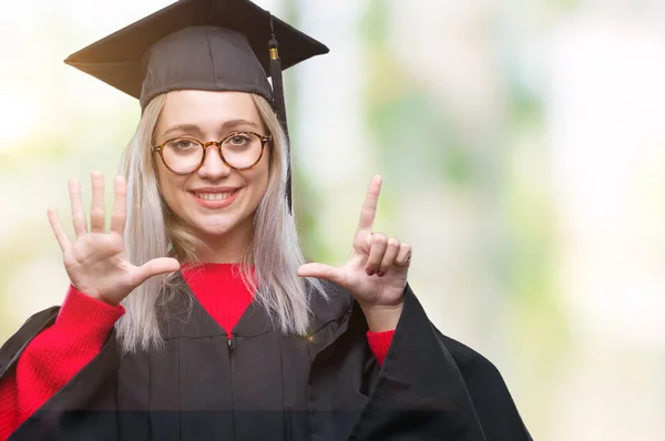 年轻的金发女子穿着毕业制服在孤立的背景显示 并指出手指七 而微笑着自信和快乐 — 图库照片