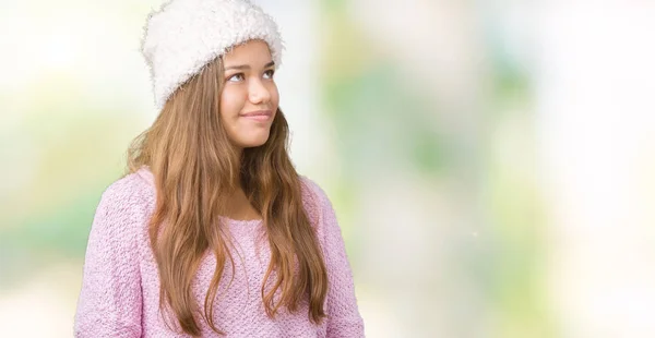 年轻美丽的黑发女人穿着毛衣和冬帽在孤立的背景看着一边面带微笑 自然的表情 笑自信 — 图库照片