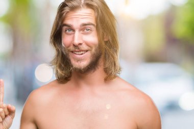 Genç yakışıklı gömleksiz adam uzun saçlı seksi vücut üzerinde izole arka plan işaret parmağı ile başarılı fikir göstermek yukarıya. Çıktıktan ve mutlu. Bir numara.