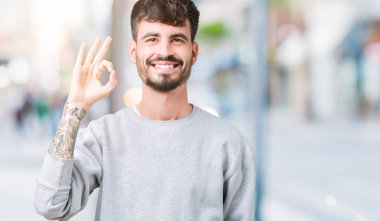 Genç yakışıklı adam izole arka plan el ve parmaklar ok işaretiyle yapıyor olumlu gülümseyen üzerinde kazak giyiyor. Başarılı ifade.