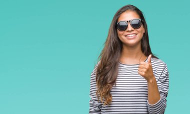 Genç güzel Arap kadın hareketi el ile mutlu yaşasın yapıyor izole arka plan üzerinde güneş gözlüğü takıyor. Kameraya bakarak başarı gösteren ile ifade onaylama.