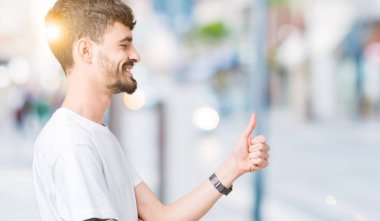 Yanına bir jest yapıyorsun gülümseyen gurur, seyir izole arka plan üzerinde beyaz t-shirt giyen genç yakışıklı adam yaşasın