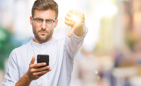 年轻英俊的男人发短信使用智能手机在孤立的背景与愤怒的脸 显示不喜欢大拇指的负面标志 拒绝的概念 — 图库照片