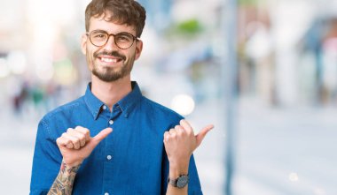 Yakışıklı delikanlı üzerinde gözlük takan izole arka plan emin gülümseyen arkasından el ve kadar başparmak ile işaret