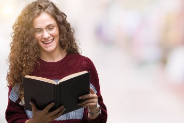 Genç esmer kız gözlüklü izole arka plan üzerinde duran ve diş gösterilen kendine güvenen bir gülümsemeyle gülümseyerek mutlu bir yüz ile bir kitap okuma