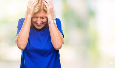 Orta yaş sarışın kadın izole arka plan çünkü umutsuz ve stresli baş ağrısı acı yüzünden acı ve migren. Ellerini kafasına.