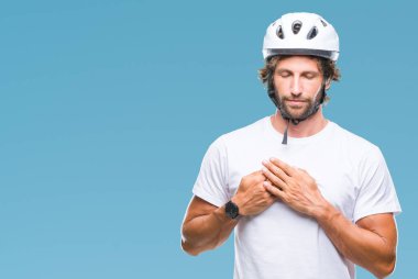 Üzerinde güvenlik kask giymiş yakışıklı İspanyol bisikletçi adam arka plan ile kapalı gözler göğüs ellerinde ve yüzünde minnettar jest ile gülümseyen izole. Sağlık kavramı.