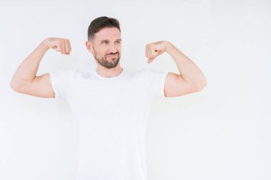 Kol kasları gururlu gülümseyen gösterilen izole arka plan üzerinde rahat beyaz t-shirt giyen genç yakışıklı adam. Fitness kavramı.