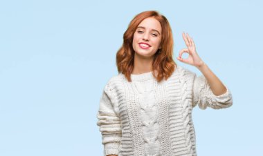 İzole arka plan el ve parmaklar ok işaretiyle yapıyor olumlu gülümseyen kış kazak giyen genç güzel kadın. Başarılı ifade.