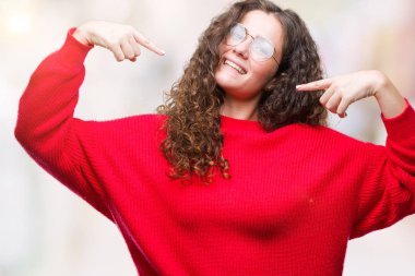 Yüzünde gülümseme ile kendinden emin görünüyorsun, kendini gururlu ve mutlu parmakları ile işaret izole arka plan üzerinde gözlük ve kış kazak giyen güzel esmer kıvırcık saçlı Genç kız.