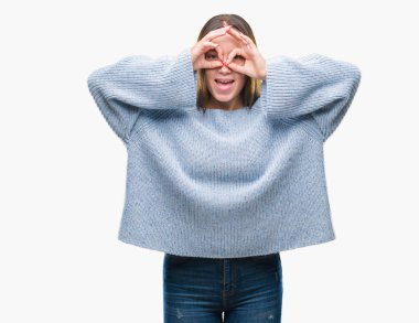 Dilini, parmaklarının arasından baktığını yapışmasını dürbün gibi ok jest yapıyor izole arka plan üzerinde kış kazak giyen genç güzel beyaz kadın. Deli ifade.