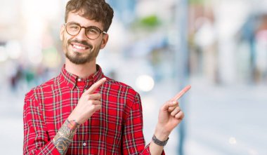 Gülümseyen ve iki elleri ve parmakları ile tarafına işaret kamera bakarak izole arka plan üzerinde gözlük takan genç yakışıklı adam.