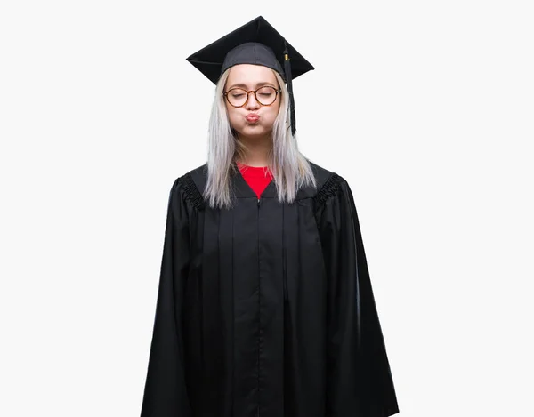 年轻的金发女子穿着毕业制服在孤立的背景下 膨化脸颊与滑稽的脸 嘴巴充气 疯狂的表情 — 图库照片