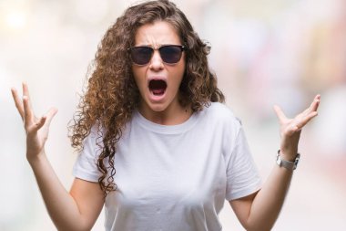 Güzel esmer kıvırcık saçlı Genç kız izole arka plan çılgın ve kızgın bağırarak ve agresif ifade ve silah kaldırdı bağırmaya üzerinde güneş gözlüğü takıyor. Hayal kırıklığı kavramı.
