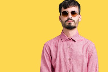 Genç yakışıklı adam yüzünde ciddi bir ifade ile izole arka plan üzerinde güneş gözlüğü takıyor. Basit ve doğal kameraya bakıyor.