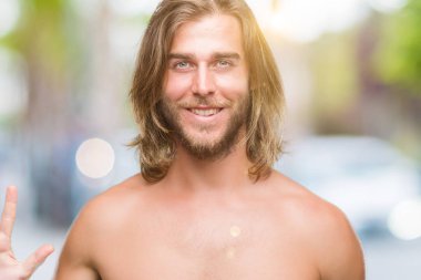 Genç yakışıklı gömleksiz adam uzun saçlı seksi vücut gösterilen ve parmakları ile işaret izole arka plan üzerinde gösterilen beş kendinden emin ve mutlu gülümseyerek iken numara.