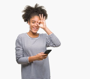 Mutlu yüz el parmaklarının arasından seyir göz üzerinde ok işaretiyle yapıyor gülümseyen izole arka plan üzerinde Smartphone kullanarak genç afro Amerikalı kadın manifatura